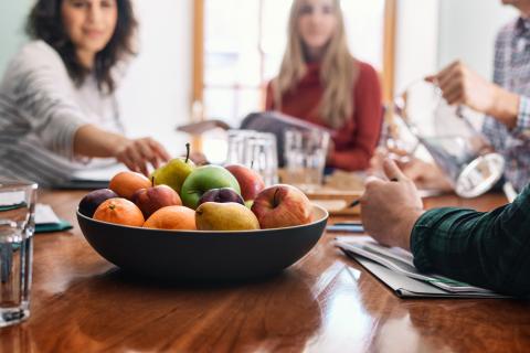 Bowl of mixed fruit on the table, surrounded by group of people.